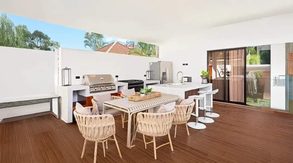 Cuisine extérieure moderne sous pergola avec îlot central équipé barbecue intégré