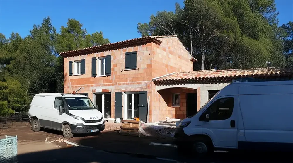 Chantier de construction d'une maison individuelle en cours de finition avec murs en briques apparent et toiture tuiles terre cuite