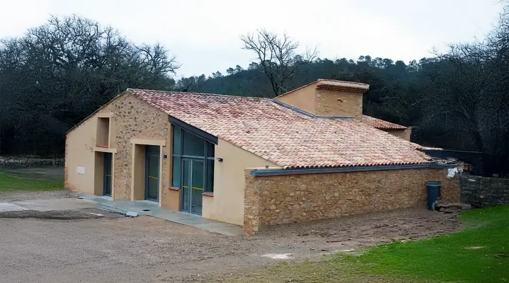 Chantier de construction d'une maison individuelle en cours d'achèvement, style traditionnel avec murs en pierre apparente et crépi beige