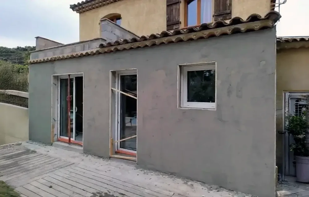 Piscine rectangulaire extérieure avec terrasse en bois, transats beiges disposés autour du bassin, pergola blanche moderne sur la droite