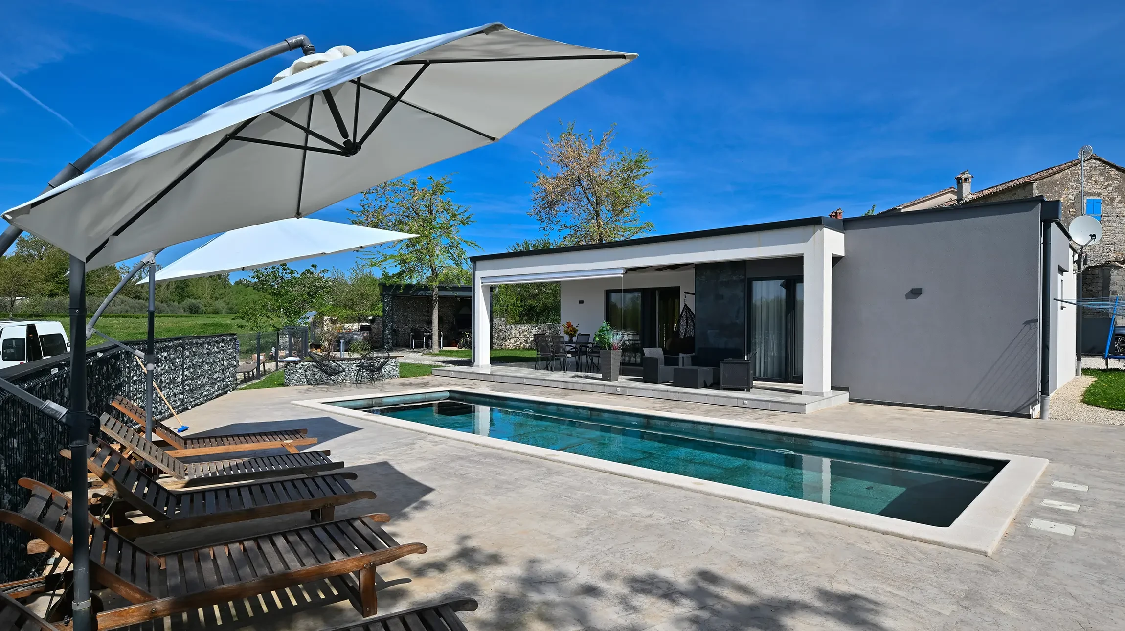 Terrasse ext&eacute;rieure am&eacute;nag&eacute;e avec salon de jardin en bois teck comprenant canap&eacute; deux places, deux fauteuils assortis avec coussins beiges, table basse carr&eacute;e massive